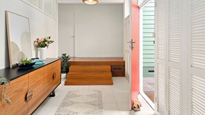 A hallway with a wooden floor, a black countertop with a bowl of flowers, a white door, and a staircase leading to a balcony. - Elegant 4BR Sanctuary with Private Pool (Warrawee)