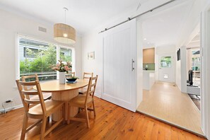 Een moderne eetruimte met een houten tafel en stoelen, een potplant en een schuifdeur die naar een keuken leidt.