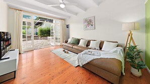 A living room with a brown sofa, a white coffee table, a TV, and a plant. - Elegant 4BR Sanctuary with Private Pool (Warrawee)
