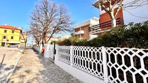 A street with a white lattice fence, a yellow building, and a modern building with a red and white facade. - Casa Marina [30 mt from the sea, wifi, park, seaview] (Marcelli)