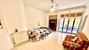 A living room with a dining area, a sofa, a ceiling fan, and a window with blinds. - Large quadrilo with p.auto and a/c near the sea (Marcelli)