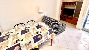 A dining area with a table covered in a patterned tablecloth, a black and white sofa, a lamp, and a TV in the background. - Large quadrilo with p.auto and a/c near the sea (Marcelli)