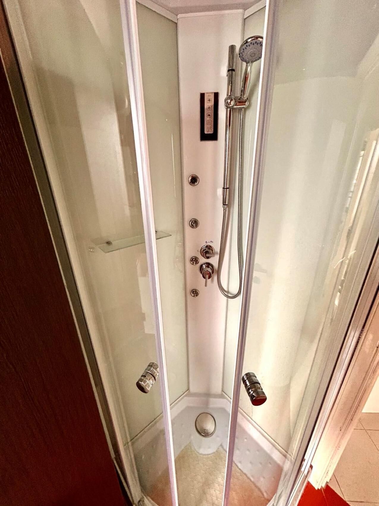 A glass-enclosed shower stall with a handheld showerhead and a wall-mounted faucet.