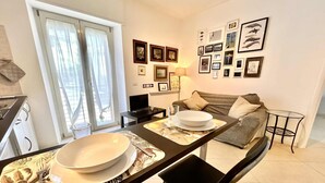 Ein modernes Wohnzimmer mit Sofa, Esstisch, Geschirr und Besteck, einem Fernseher und gerahmten Bildern an der Wand.