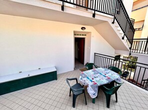 Eine überdachte Terrasse im Freien mit Tisch und Stühlen, einer Treppe und einer Tür zu einem Innenraum.