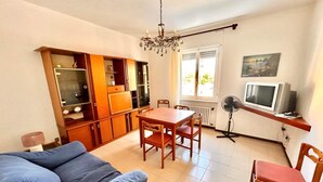 Una sala de estar con sofá, mesa de comedor, sillas, candelabro, televisor y aparador.