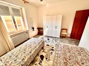 Ein Schlafzimmer mit zwei Betten, einem Kleiderschrank, einem Heizkörper und einem Fenster mit Jalousien.