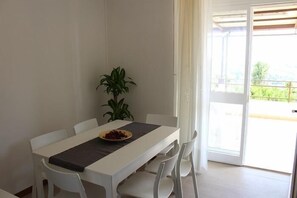 Un coin repas avec une table blanche, un chemin de table noir et un saladier rempli de nourriture. Une plante en pot est posée sur la table.