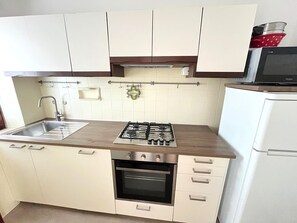 Une cuisine équipée d’une cuisinière à gaz, d’un four, d’un évier et de meubles de rangement blancs.