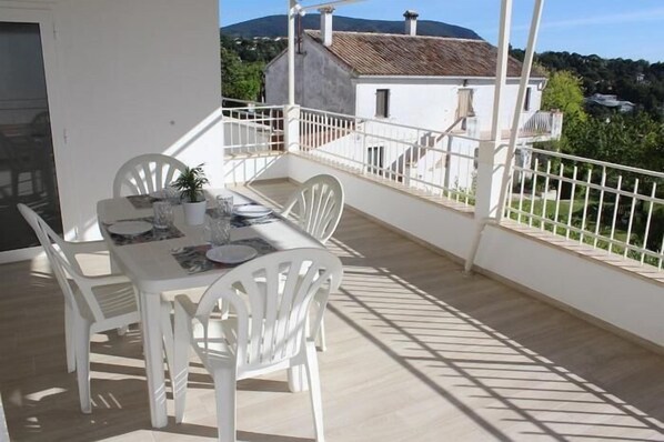 Un balcon avec une table dressée pour le repas, des chaises blanches et une plante en pot.