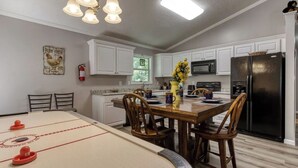 A kitchen with white cabinets, a black refrigerator, a wooden dining table, and a ping pong table. - A 2-bedroom Hillbilly Getaway house surrounded by charming nature. (Sevierville)