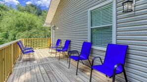 A wooden deck with blue chairs and a wooden railing. - A 2-bedroom Hillbilly Getaway house surrounded by charming nature. (Sevierville)