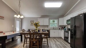 A kitchen with white cabinets, a black refrigerator, and a dining table with chairs. - A 2-bedroom Hillbilly Getaway house surrounded by charming nature. (Sevierville)