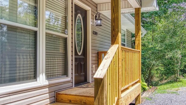 A wooden front porch with a bench, a door with a glass panel, and a mailbox. - A 2-bedroom Hillbilly Getaway house surrounded by charming nature. (Sevierville)