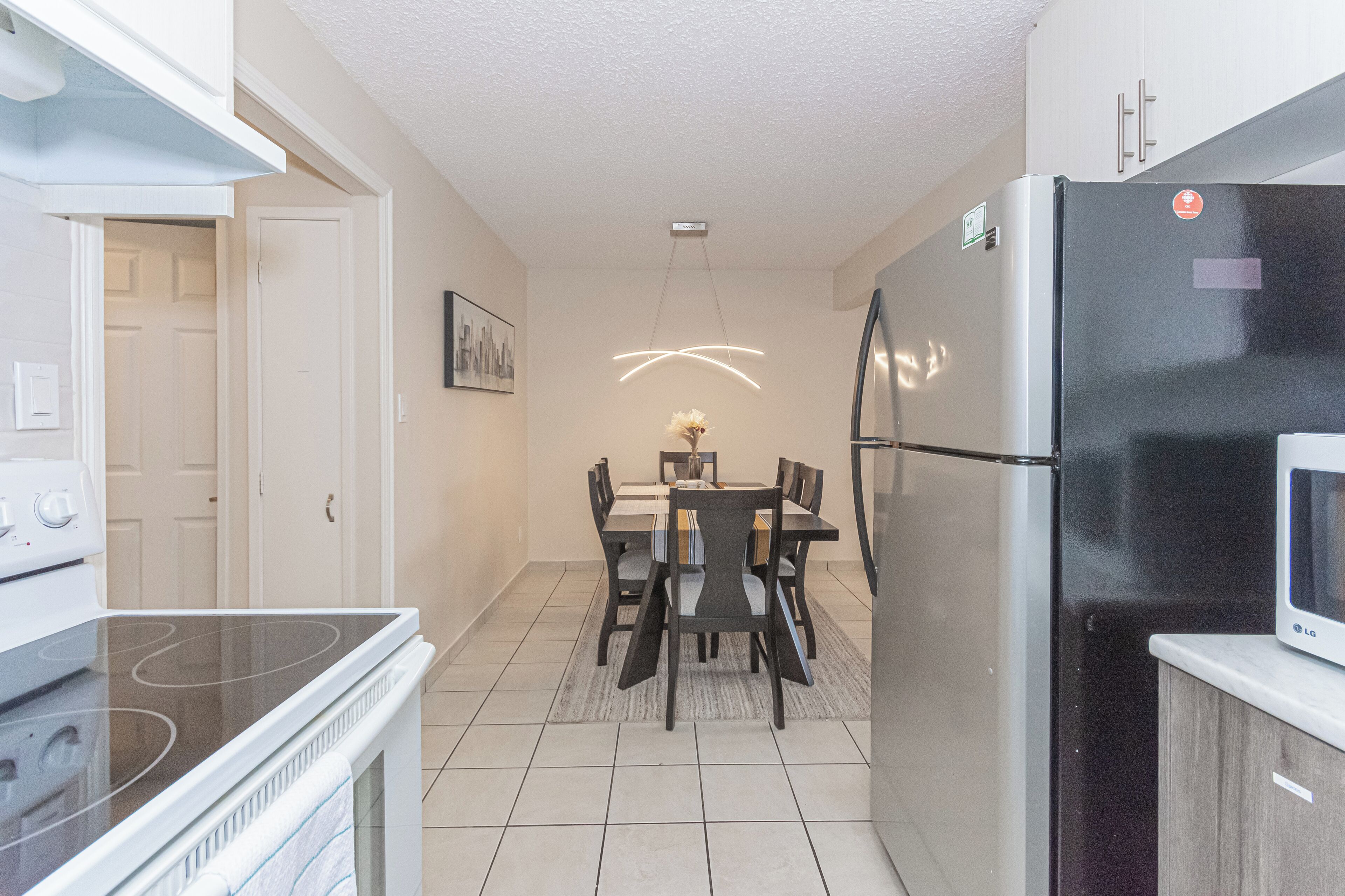 A kitchen with a stove, refrigerator, dining table, chairs, and a hanging light fixture.
