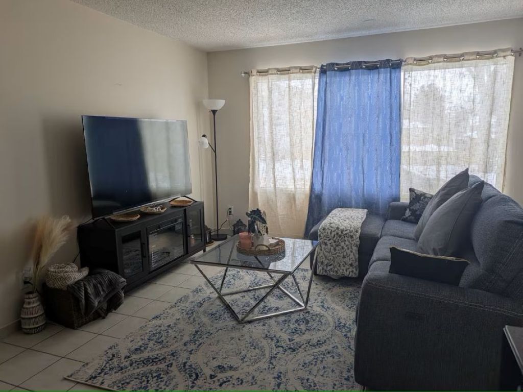 Ein Wohnzimmer mit Flachbildfernseher, einer Couch, einem Couchtisch und einer Lampe.