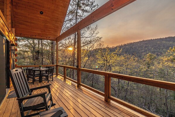 Eine Holzterrasse mit Tisch und Stühlen, mit Blick auf eine bewaldete Landschaft.