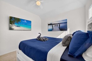 A bedroom with a bed, a ceiling fan, and two wall-mounted paintings.