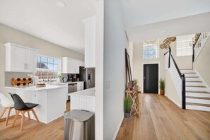 A modern kitchen with white cabinetry, a central island, and a dining area with a black chair.