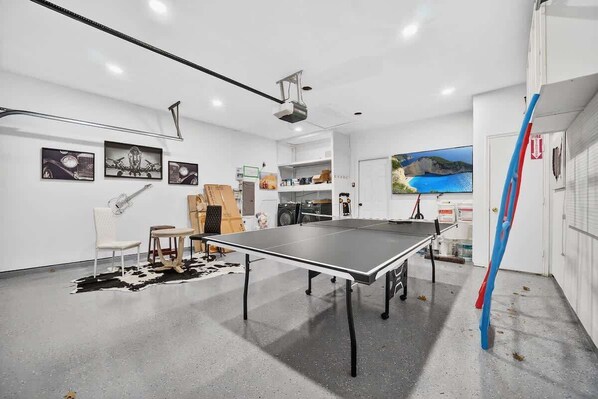 A room with a ping pong table, white walls, and various artworks.