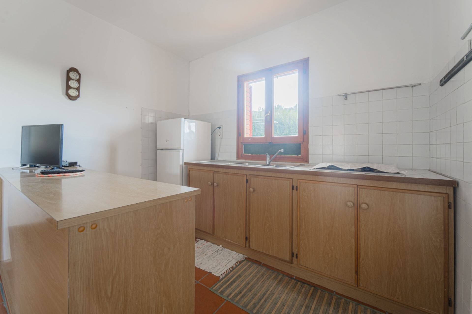 Una cocina con armarios de madera, un refrigerador blanco, una ventana con marco rojo y un salpicadero de azulejos.