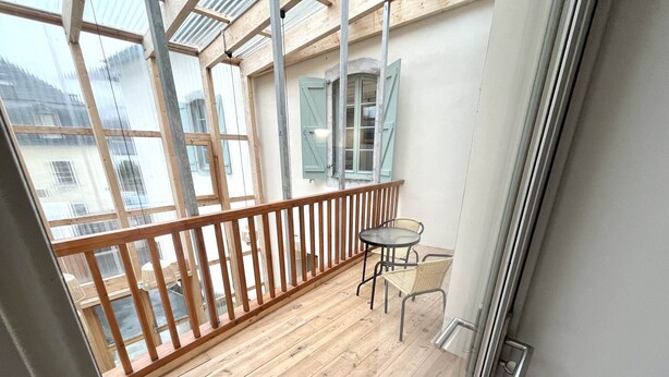 Een balkon met houten vloer, een glazen deur en een klein tafeltje met twee stoelen.