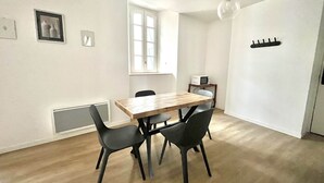 Een eethoek met een houten tafel en vier stoelen, een raam, een magnetron en een plafondlamp.