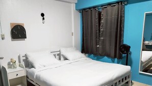 Ein Bett mit weißer Bettwäsche, ein Nachttisch mit einer Vase, eine Wandleuchte und ein Fenster mit dunklen Vorhängen.