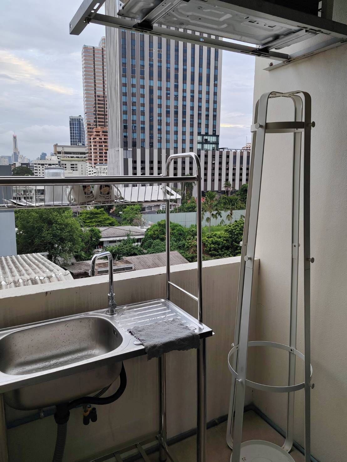 Un balcón con un pileta de acero inoxidable, una escalera y vistas de un paisaje urbano con edificios altos.