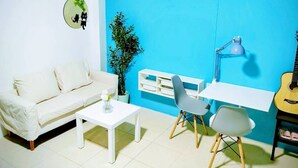 Une pièce avec un mur d’accent bleu, un canapé blanc, une petite table blanche, une chaise grise, un bureau avec une lampe et une guitare.