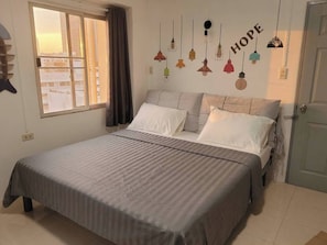 A bedroom with a bed, a window with curtains, and a wall with hanging lights. - Stay with Ease at Grand Residence 12 (Bangkok)