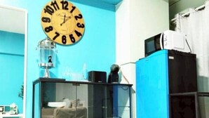 Une pièce avec un mur bleu, une horloge ronde, une vitrine, un réfrigérateur bleu et un tapis gris.