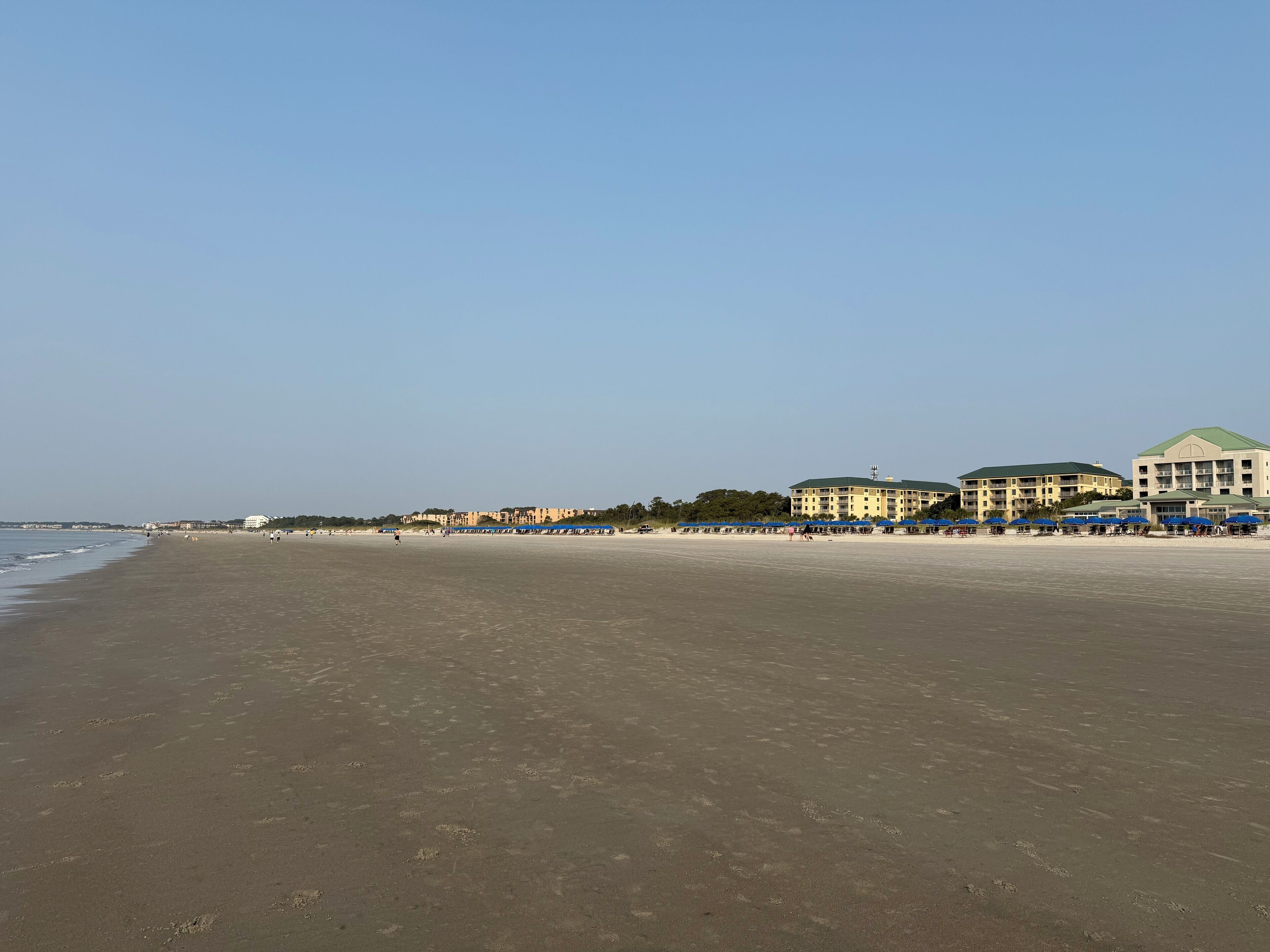 En strand med en rad blå parasoller och en byggnad med ett grönt tak i bakgrunden.