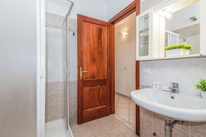 Ein Badezimmer mit Holztür, einer Duschkabine aus Glas, einem Waschbecken mit Spiegel und einer Topfpflanze.