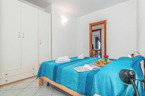 A bedroom with a bed, a wardrobe, a bedside table with a lamp, and a mirror. - Tavolara Sea View Apartments (San Teodoro)