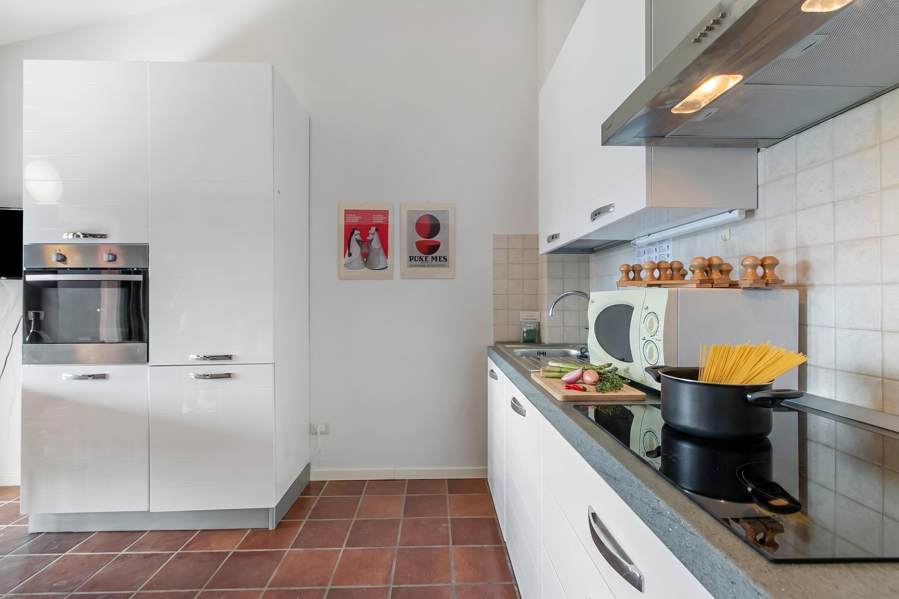 Una cocina moderna con armarios blancos, horno empotrado, microondas y una olla de espagueti sobre la encimera.