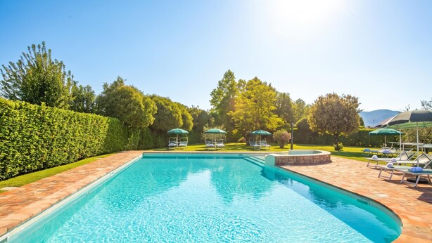A rectangular swimming pool with a tiled deck, surrounded by a well-maintained hedge and trees. - Cosy House Serena- Park & Shared Pool (Puegnago del Garda)