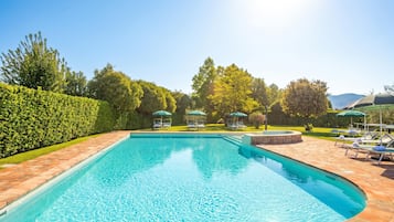 Piscina retangular com deck ladrilhado, rodeada por um conjunto de sebe bem cuidado e árvores.