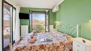 A bedroom with a bed, a nightstand, a TV, and a balcony view. - Cosy House Serena- Park & Shared Pool (Puegnago del Garda)