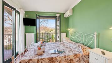 Quarto com cama, mesa de cabeceira, televisão e vista para a varanda.