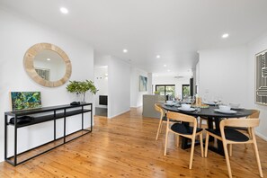 A modern dining area with a round table, wooden chairs, a black console table, and a large mirror on the wall.