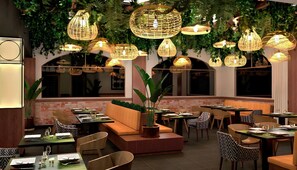 A restaurant with multiple tables and chairs, hanging wicker lamps, and a brick wall.
