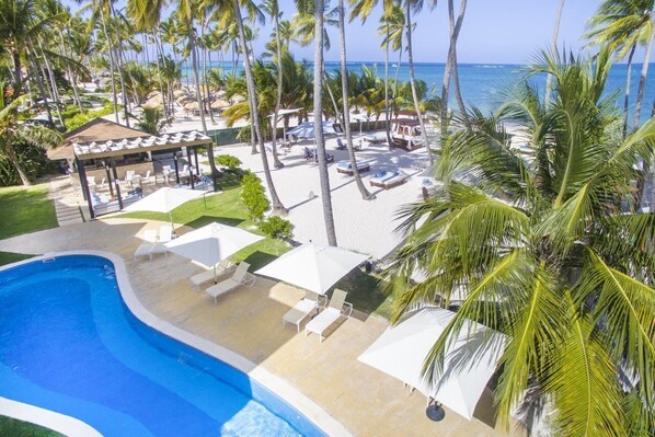 Un complexe hôtelier doté d’une piscine, de chaises longues, de parasols et d’une plage bordée de palmiers.