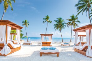 A beach resort with wooden cabanas, white beds, and palm trees. - Sunscape Coco Punta Cana (Punta Cana)