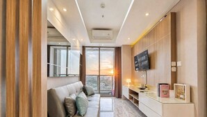 Ein modernes Wohnzimmer mit einer Couch, einem Fernseher und einem Schreibtisch mit Lampe und Büchern.