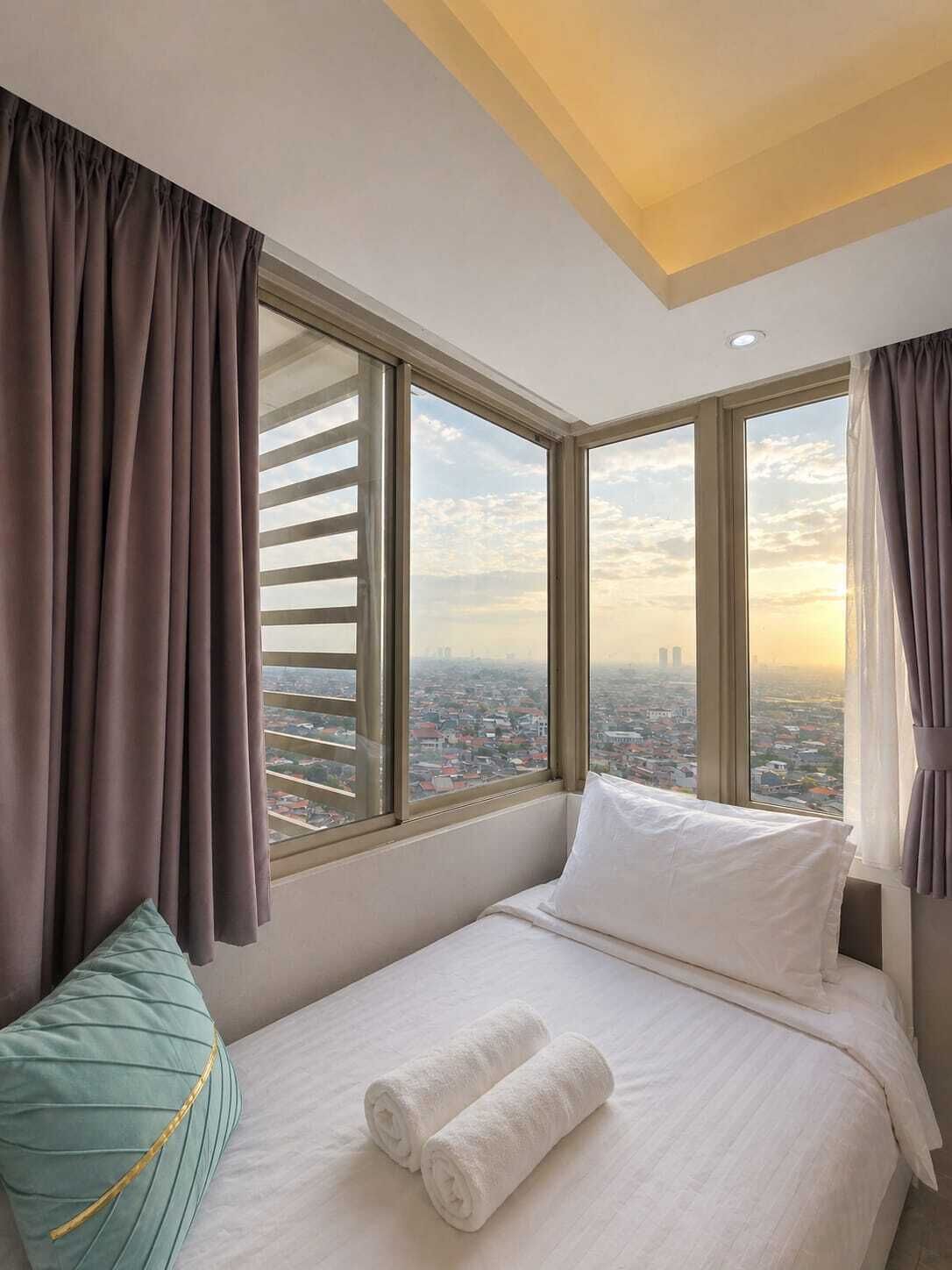 Habitación de hotel con una cama grande, dos almohadas, vistas de la ciudad y una ventana con persianas.