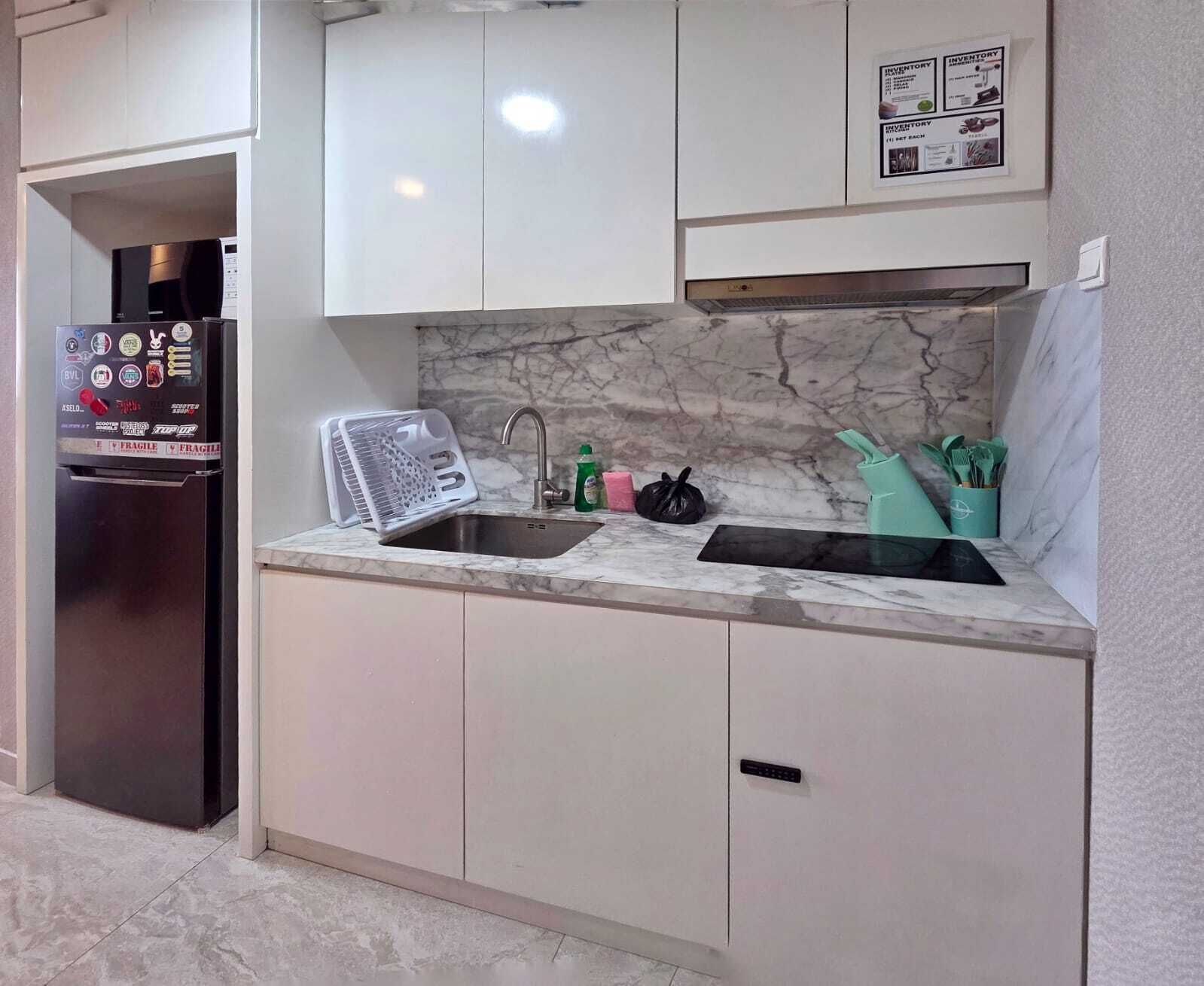 Cozinha com painel de parede em mármore, pia de aço inoxidável e geladeira com etiquetas de segurança.