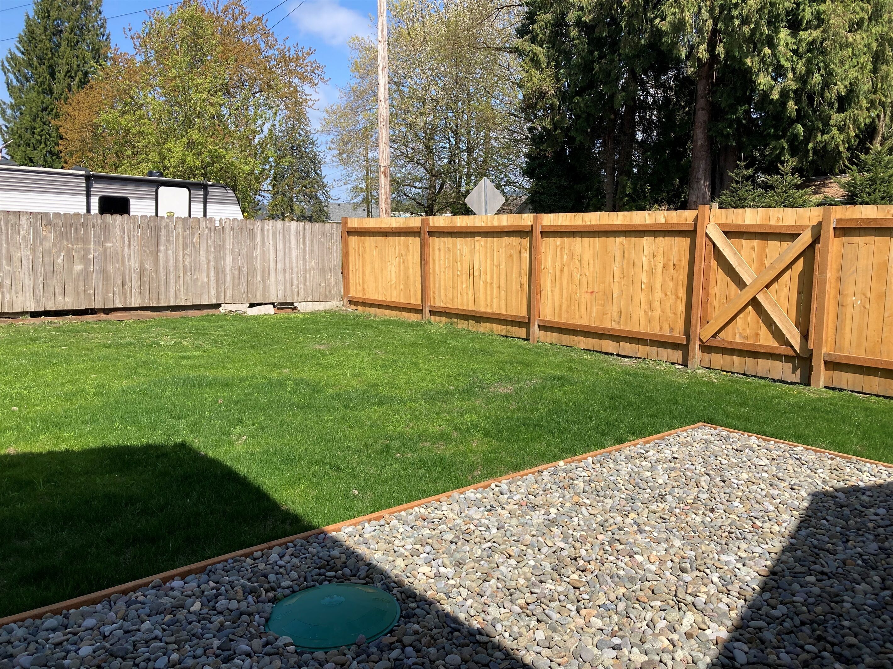 A backyard with a wooden fence, a gravel area, and a grassy lawn.