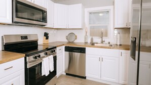 A modern kitchen with white cabinets, stainless steel appliances, a dishwasher, and a window with blinds. - Updated 3 Bedroom Charmer (Kelso)