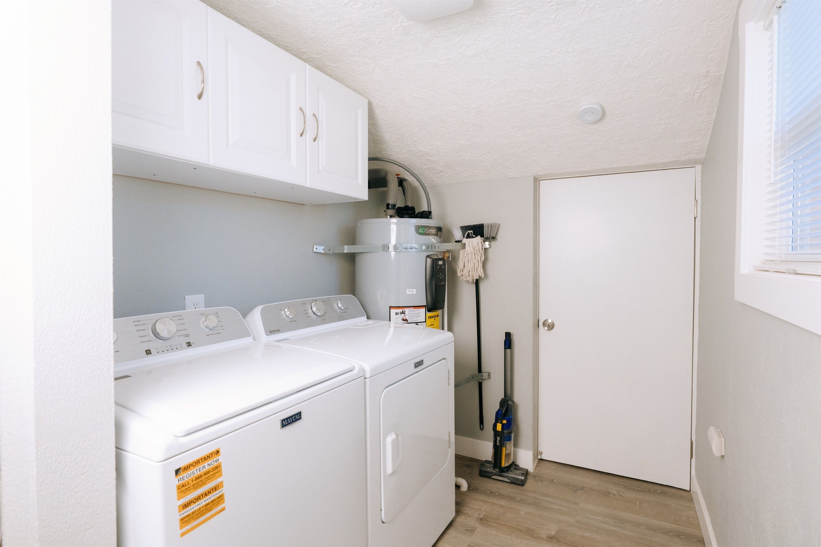 A laundry room with two front-loading washing machines, a dryer, and a water heater.